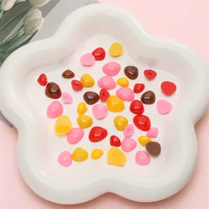 Mix of colorful heart and pebble shaped resin accessories for DIY craft on a white tray