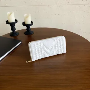 Elegant white quilted long wallet with V-shaped stitching and gold zipper on wooden table