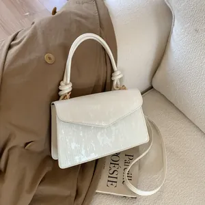 Cream envelope crossbody bag with vertical texture and stylish knot handle on a trench coat
