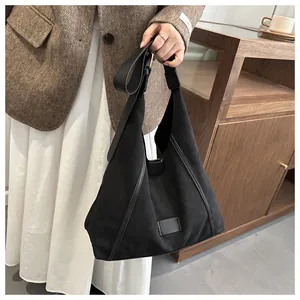 Close-up of a large black matte tote bag held by a model in a cozy interior setting