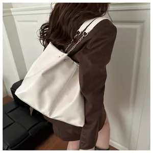 Detail of cream white leather tote bag with gold chain strap on model shoulder
