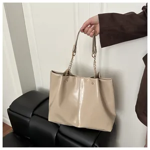 Detail view of glossy beige leather tote bag featuring gold rivets and chain strap