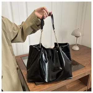 Detail of glossy black oil wax leather tote bag with gold chain strap in a lifestyle setting