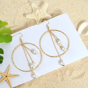 Elegant gold hoop tassel earrings with white pearls on a tropical beach background
