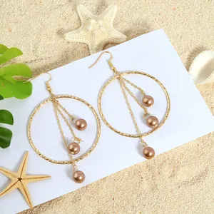 Detail of gold hoop earrings with tiered champagne pearl tassels on a beach background