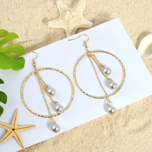 Detail view of golden tassel earrings with round hammer-textured rings and white pearls