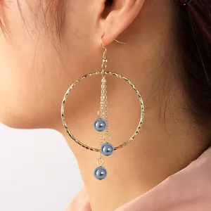 Detail of gold hammered hoop earrings with tassels and grey pearls on model