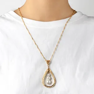 Detail van de druppelvormige ketting met drie witte parels op een gouden ketting met textuur