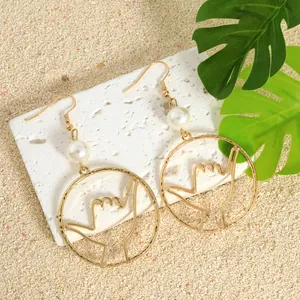 Gold Hawaii hand gesture pearl drop earrings on a tropical beach vacation background