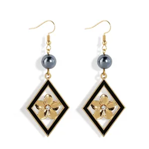 Détail de boucles d'oreilles losange avec émail noir, fleur dorée et perle de nacre