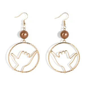 Close-up of golden Shaka hand gesture earrings with brown pearl bead on white background