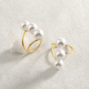 Dettaglio dell'anello aperto dorato con tre perle bianche su una superficie di pietra