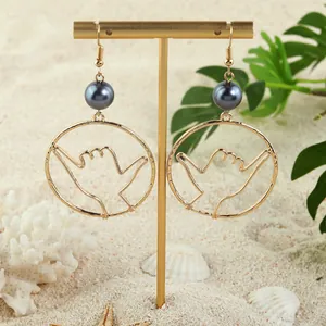 Gold Shaka hand gesture earrings with black pearl bead on tropical beach background