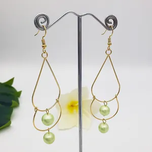 Detail of gold drop earrings with irregular metal frames and light green pearls