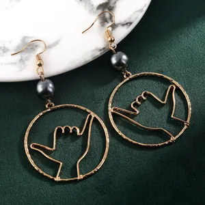 Detail of Shaka gesture golden earrings with dark grey pearl on marble surface