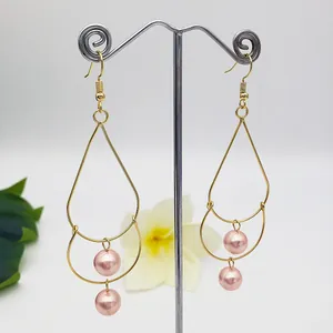 Detailed shot of double-layered teardrop pearl earrings with gold tassels on a stand