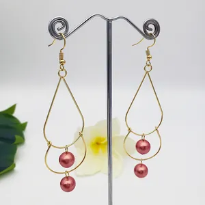 Close-up of double-layer golden teardrop earrings with elegant pink imitation pearls
