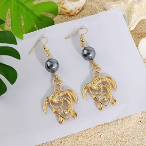 Boucles d'oreilles tortue dorées avec perle grise et coquillage sur sable