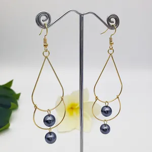 Detailed macro view of gold pear-shaped drop earrings with dual grey pearls on a display