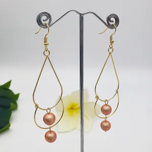 Detail of double-layer gold drop earrings with pink-orange pearls on a silver display stand