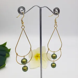 Detail of gold teardrop earrings with double green pearls on a metal display stand