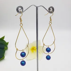Detailed close-up of gold double-layer teardrop earrings with iridescent purple beads