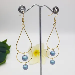 Detailed close-up of double-layer gold teardrop earrings with iridescent blue pearls