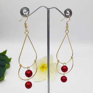 Detail of gold double-layer teardrop earrings with wine red beads on a jewelry stand