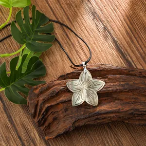 Handmade Hawaiian shell flower pendant necklace with a black cord on a rustic wood base