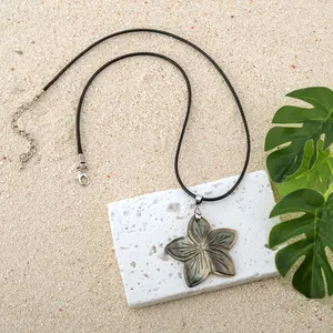 Detail of hand-carved black shell frangipani flower pendant on a black cord necklace