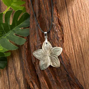 Close-up of shell turtle and flower pendant on black cord over natural wood background
