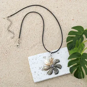 Detailed shot of mother of pearl frangipani pendant on black cord over beach sand