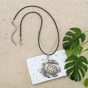 Hawaiian shell turtle pendant necklace with black cord on a beach themed background