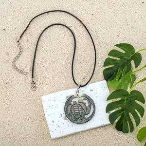 Detailed view of abalone shell turtle pendant necklace on a sandy beach setting