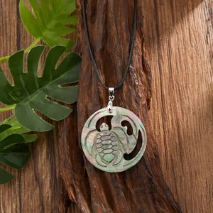 Detail of round shell turtle pendant with iridescent luster on natural wood and leaf