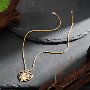 Collier classique avec pendentif cœur doré et fleur de frangipanier sur un fond de pierre