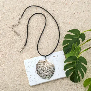 Macro detail of Monstera leaf shell pendant on black cord over sand and stone