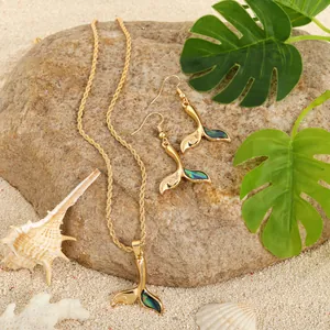 Detailed close-up of whale tail jewelry set with abalone shell on beach sand and rocks