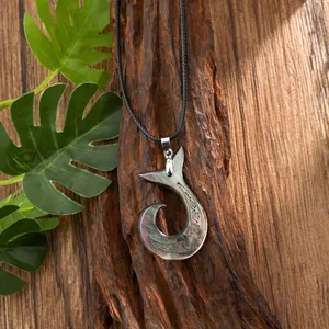 Close-up of shell fish hook pendant with tribal carvings on natural bark background