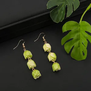 Macro shot of handmade green tulip bud earrings on a black textured background with monstera leaf