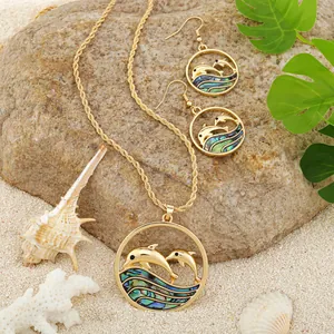 Detailed shot of golden dolphin pendants with abalone shell inlay on a beach background