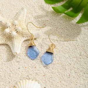 Böhmische blaue Meerglas-Ohrhänger mit Golddrahtwicklung auf weißem Sandstrand