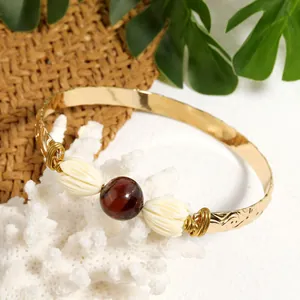 Detail of gold ethnic cuff with tiger eye stone and resin jasmine flowers on white coral