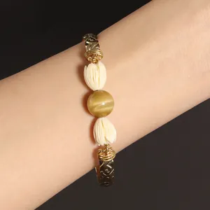 Macro detail of gold-tone floral bracelet with tiger eye stone and white resin buds