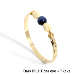Detail of gold etched bangle with dark blue tiger eye and white pikake flowers