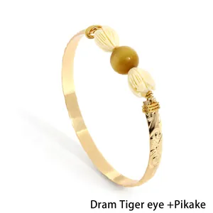 Detailed view of gold bangle featuring brown tiger eye and white Pikake jasmine beads