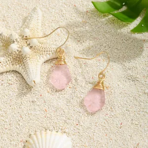 Details von rosa Tropfen-Ohrringen aus Meeresglas mit Golddraht auf weißem Strandsand