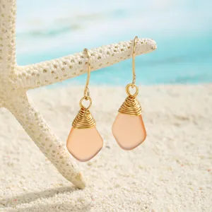 Detail handgefertigter Ohrringe mit matt orangefarbenem Meeresglas auf Strandsand