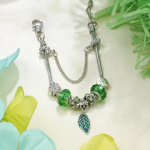 Detail of silver snake chain bracelet with green glass beads and clover charms