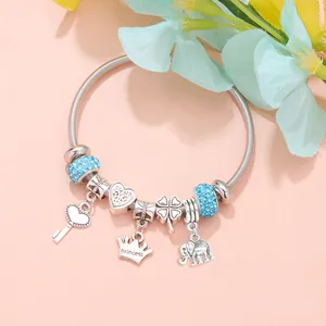 Silver charm bracelet with princess crown, heart, and blue crystal beads on pink background